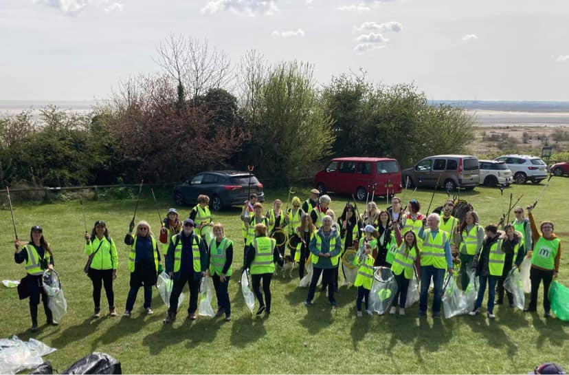 A large group of volunteers in high viz omn a gree, holding rubbish bags and waving their litter picks in the air