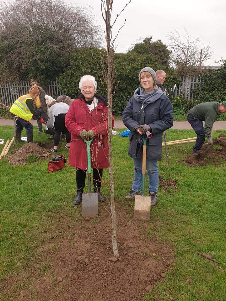 Two women leaning on spades with other volunteers digging behind them